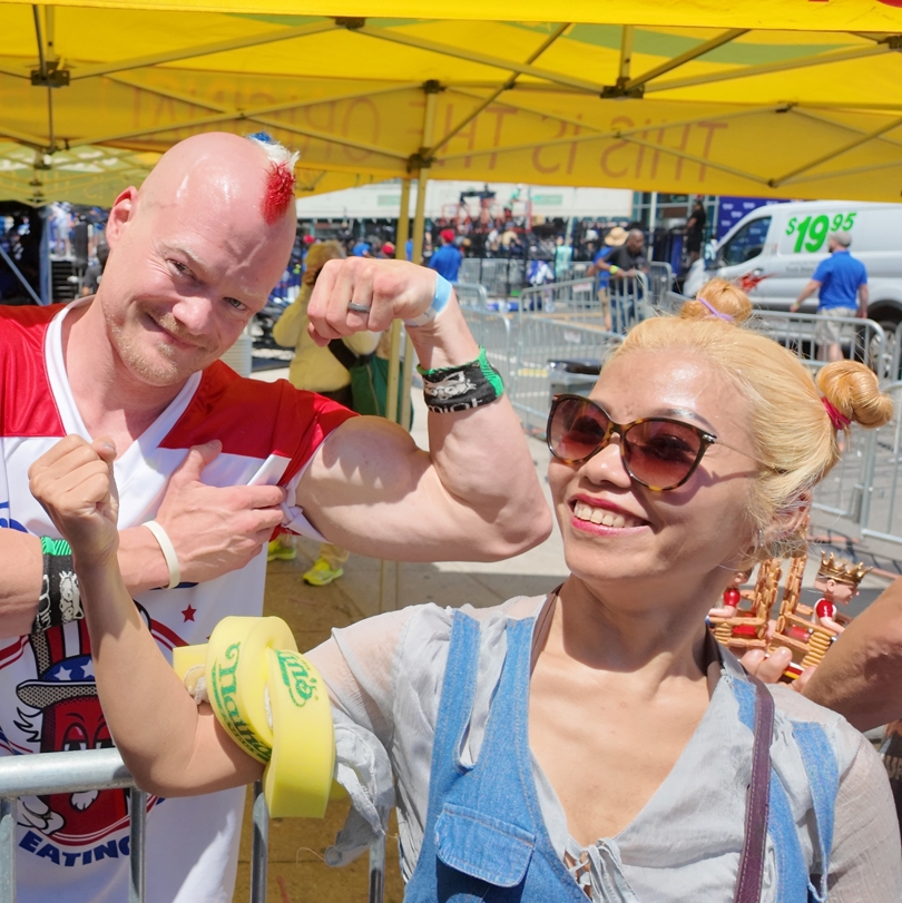 A man with a very muscular arm and a red white and blue mohawk poses with a fan