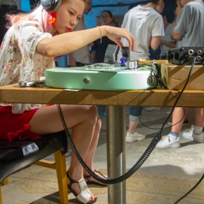 A woman with headphones sitting down touches a guitar on a table